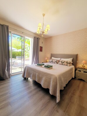 A bedroom with a large bed, a chandelier, a sliding glass door, and a nightstand with a lamp.