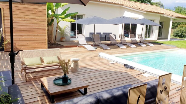 A wooden deck with a pool, lounge chairs, and umbrellas.