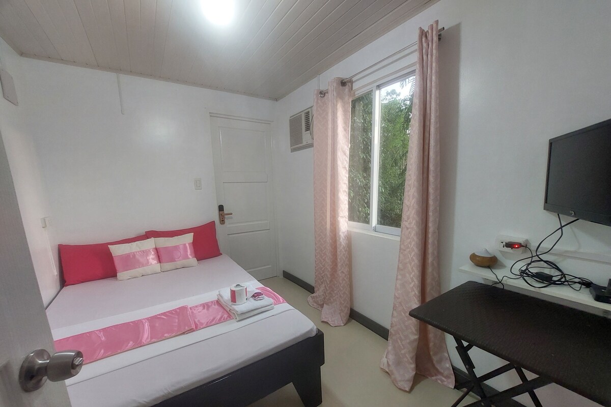 Un dormitorio con cama, escritorio, televisor y ventana con cortinas.