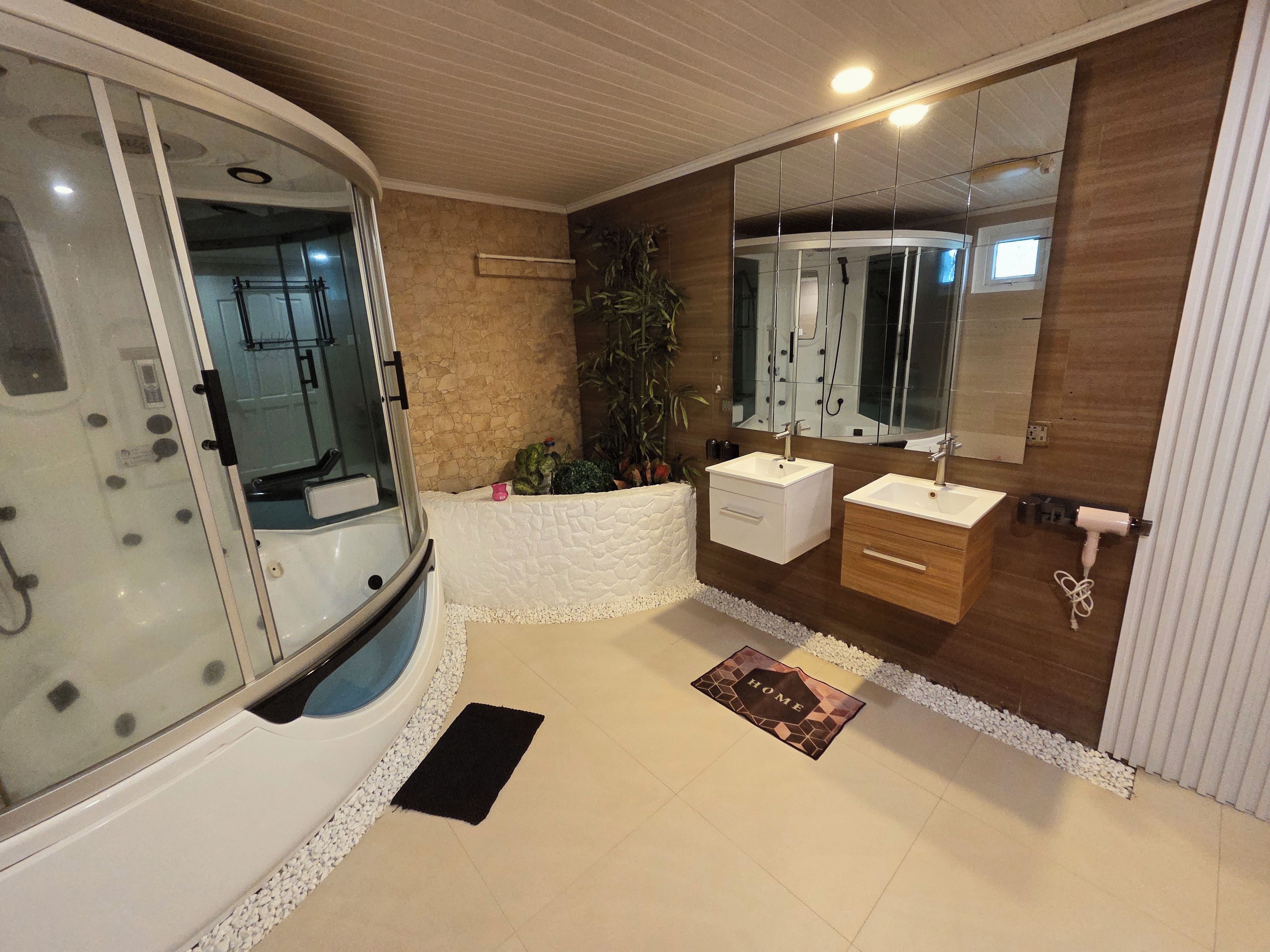 Une salle de bain moderne avec une douche à parois de verre, deux vasques, un grand miroir et un tapis décoratif.