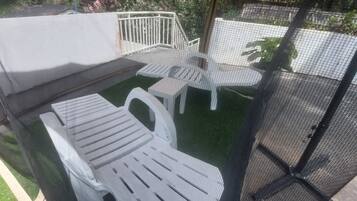 Een terras met een witte buitenbank en stoelen, omgeven door een hekwerk van gaas.