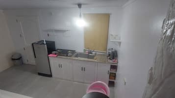 A compact kitchen with white cabinets, a stove, and a sink. There is a small window above the sink and a ceiling light fixture.