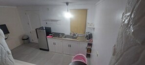 A compact kitchen with white cabinets, a stove, and a sink. There is a small window above the sink and a ceiling light fixture.