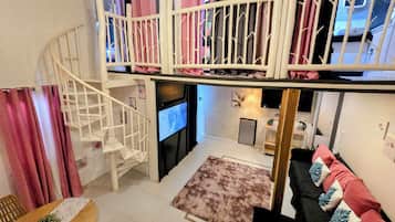 A multi-level living space with a staircase, a flat-screen TV, a kitchen area, and a sofa with decorative pillows.