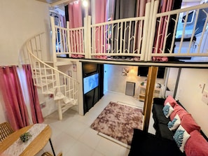 Un espace de vie à plusieurs niveaux comprenant un escalier, un téléviseur à écran plat, un coin cuisine et un canapé agrémenté de coussins décoratifs.