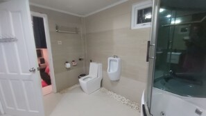 Une salle de bain comprenant des toilettes, un urinoir et une douche séparée par une paroi en verre.