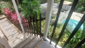 Een balkon met uitzicht op een zwembad, omgeven door weelderige begroeiing en een pad van stenen.