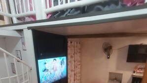 Een kamer met stapelbedden, een televisie, een klein tafeltje en een ventilator.