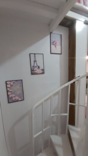 Una escalera con barandilla blanca, tres cuadros en la pared y una puerta al final.