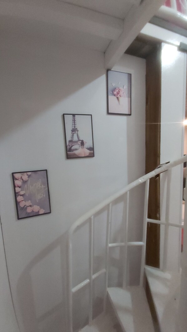 Un escalier avec une rampe blanche, trois tableaux encadrés accrochés au mur et une porte en bas.