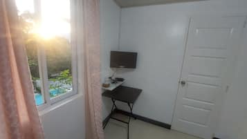 A room with a window, a flat-screen TV, a desk, and a door.