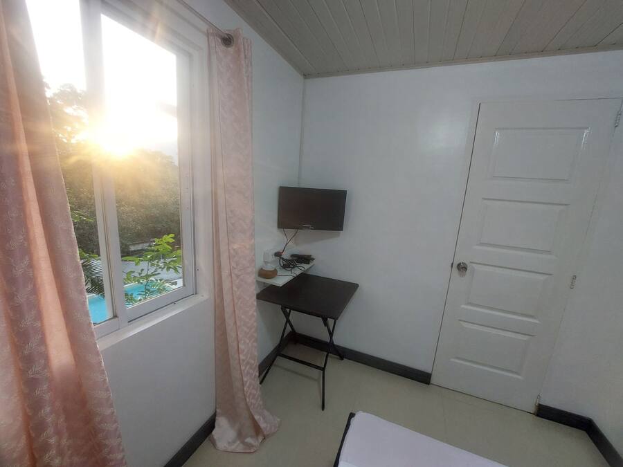 Una habitación con ventana, televisor de pantalla plana, escritorio y puerta.