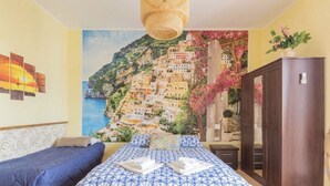 A bedroom with a bed, two bedside tables, a wardrobe, and a mural of a coastal village. - Pompei Window (Pompei)