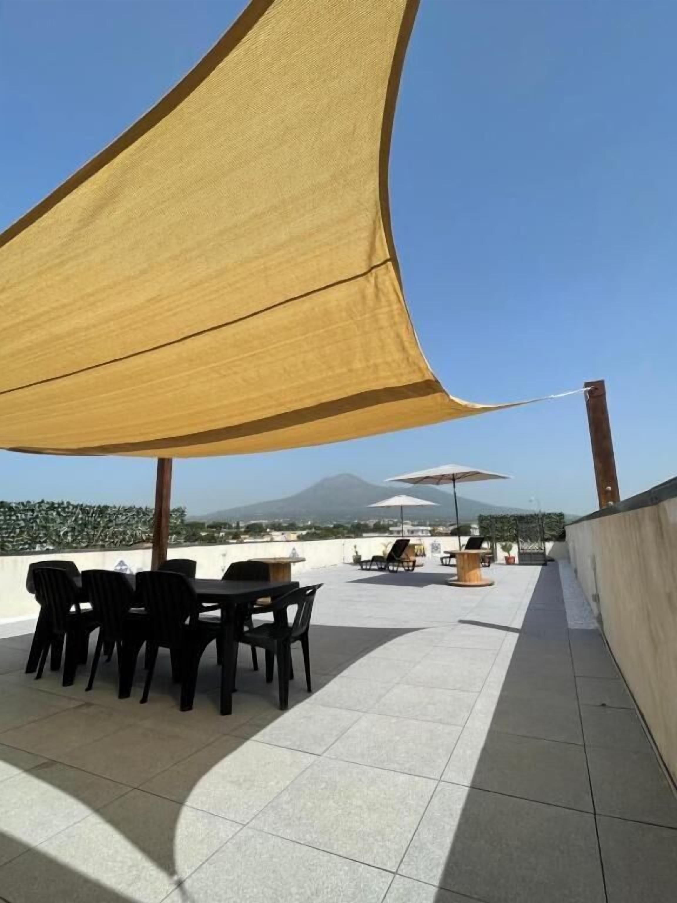 An outdoor patio with a table and chairs, a large yellow shade sail, and a mountain view in the background.