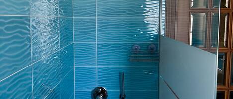 Un área de ducha con azulejos azules, un cabezal de ducha manual y una cabina de ducha con paredes de vidrio.