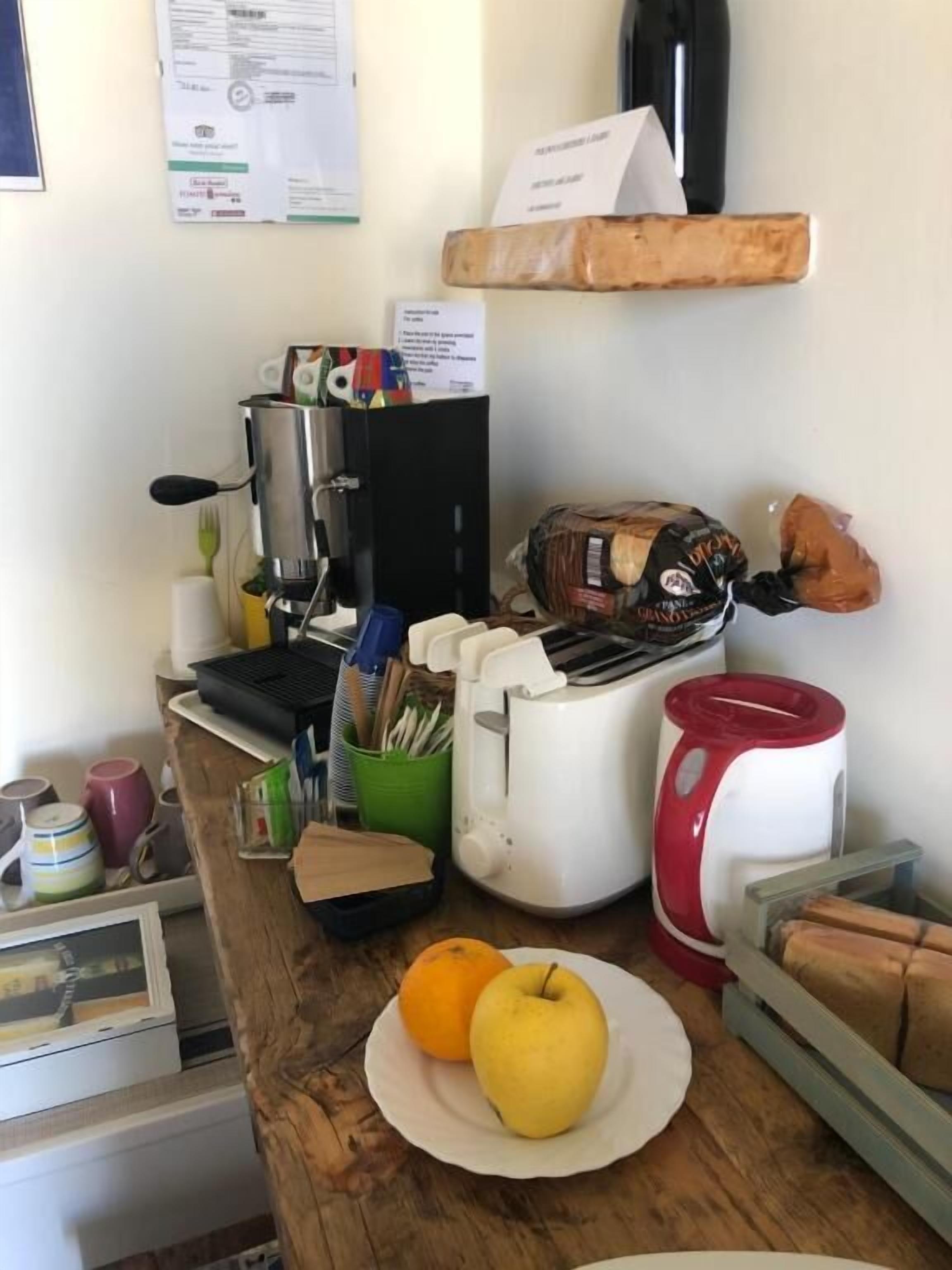 Una encimera de cocina con cafetera, tostadora, pan y frutas.