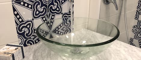 Un bagno con un lavandino in vetro, una doccia e piastrelle decorate.