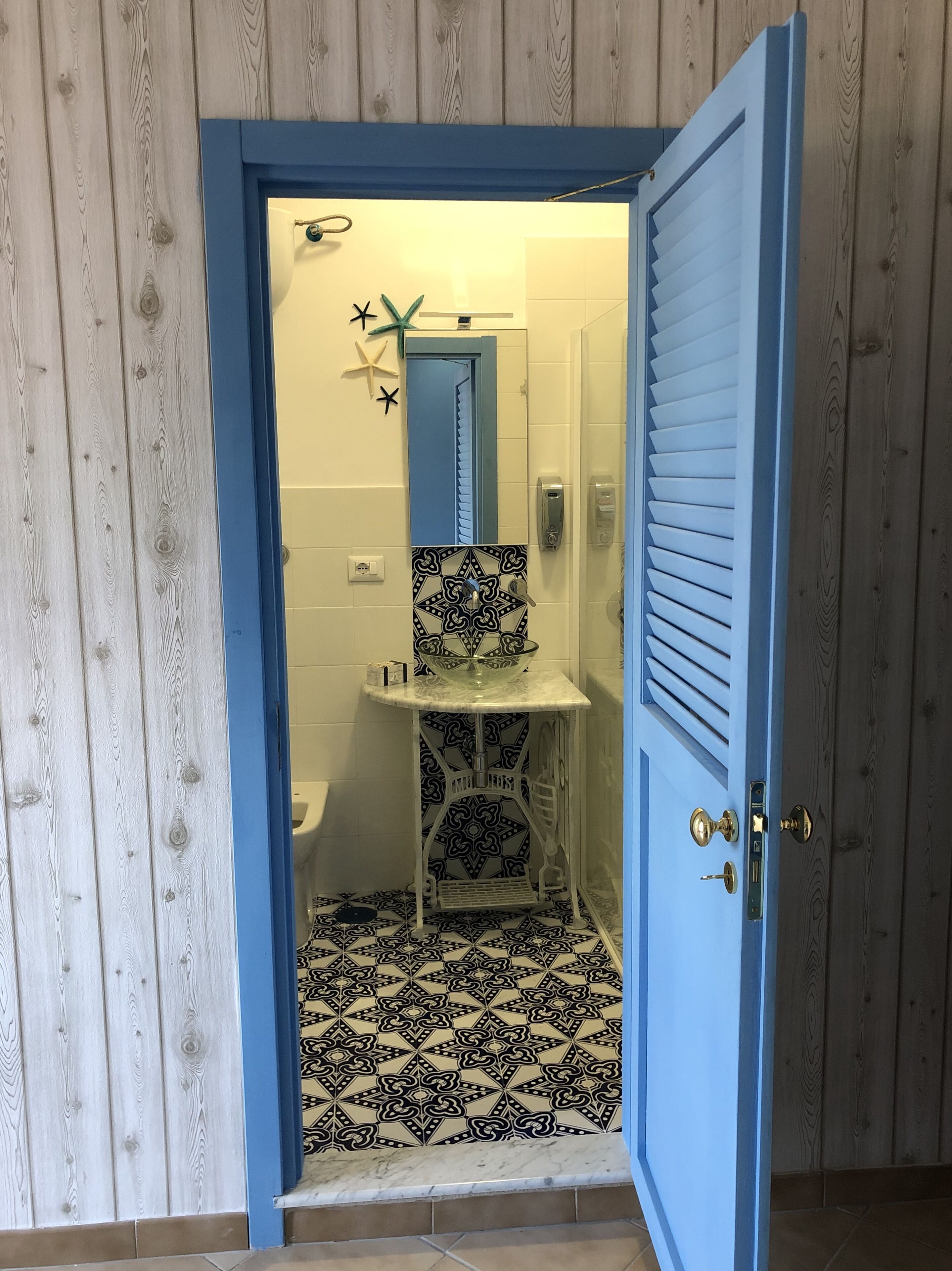 A bathroom with a blue door, a white sink, a mirror, and patterned floor tiles.