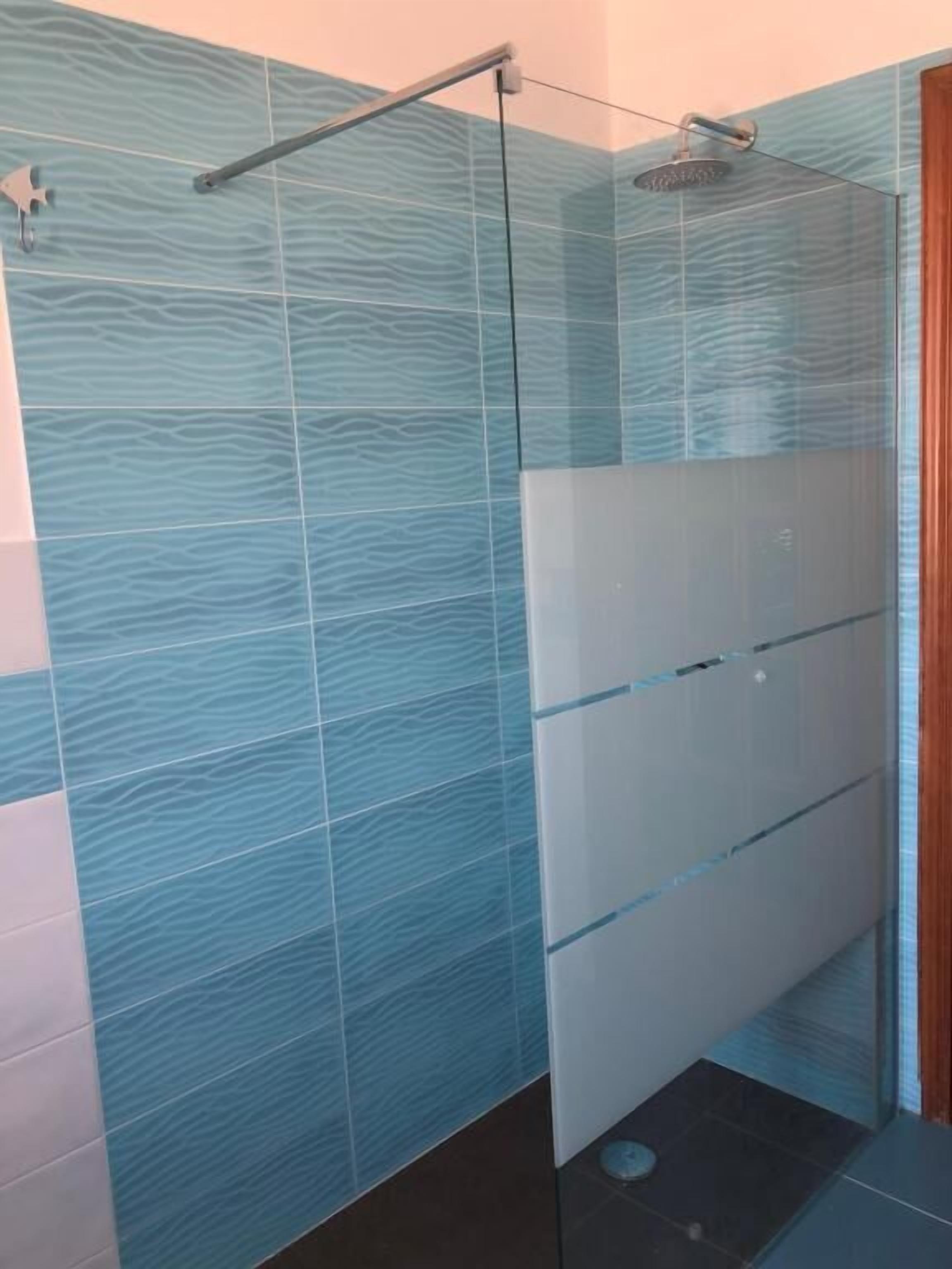 A modern bathroom with a glass shower enclosure, a glass door, and a tiled wall with a wavy pattern.