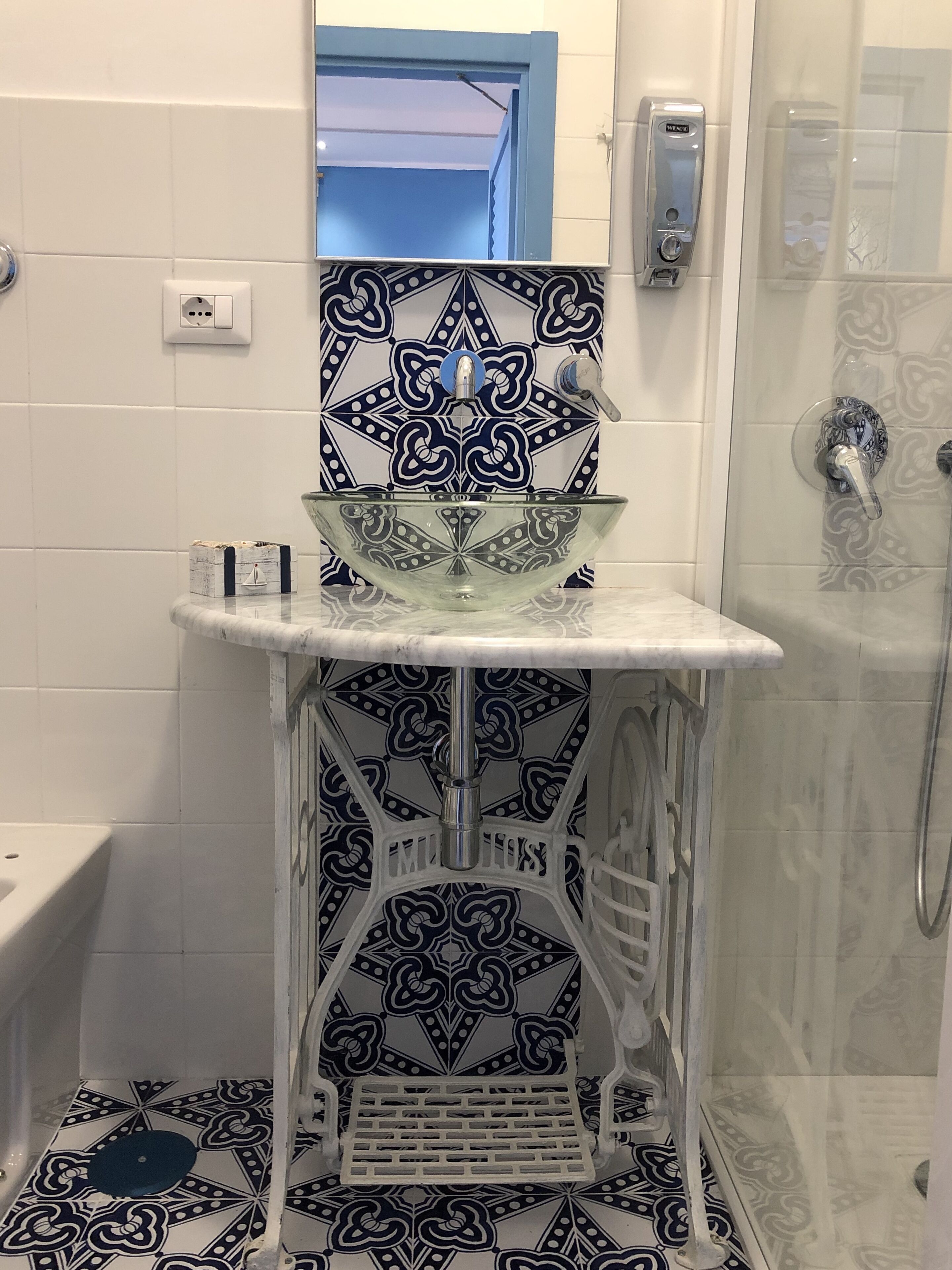 Ein Badezimmer mit einem Waschbecken aus Glas, gemusterten Fliesen, einer Dusche und einem weißen Standwaschbecken.