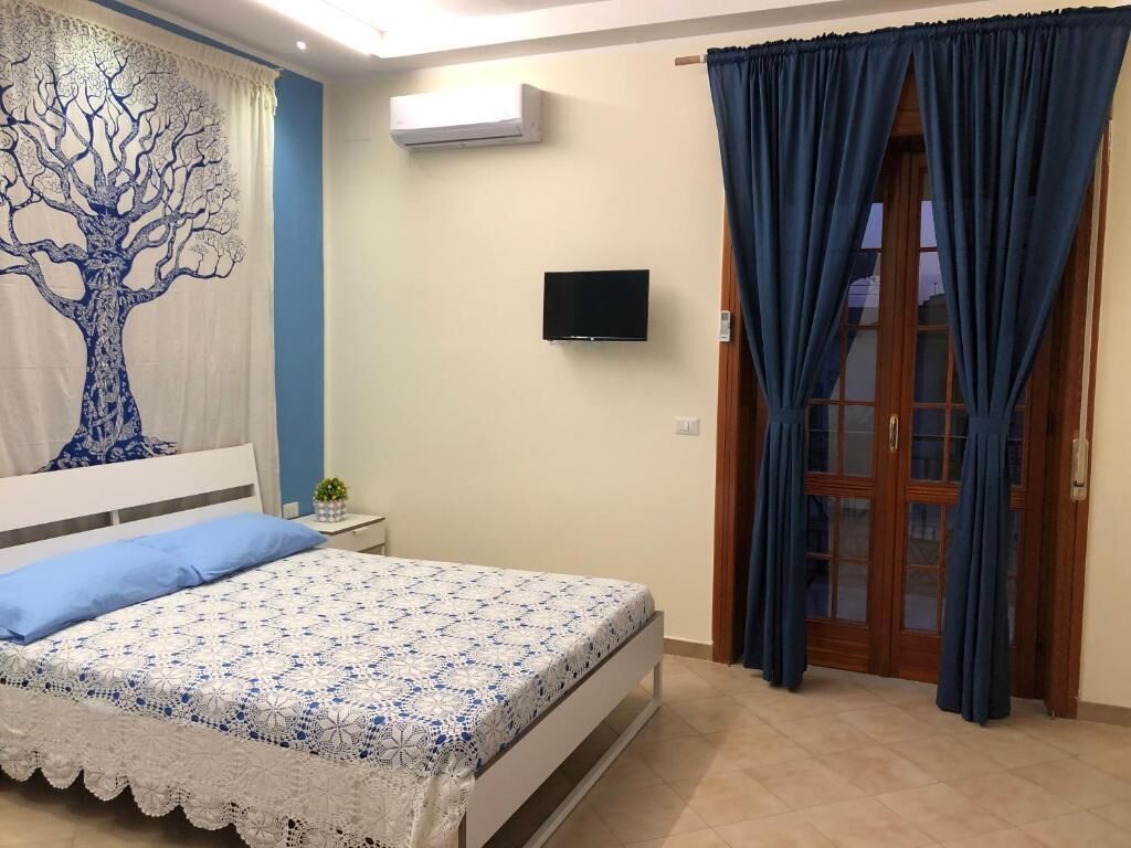 Ein Schlafzimmer mit Bett, Fernseher, Fenster mit Vorhängen und Wandgestaltung mit Baummotiv.