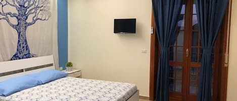 A bedroom with a bed, a TV, a window with curtains, and a wall with a tree design.