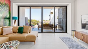 Una sala de estar moderna con un sofá, una mesa de centro, un televisor y un balcón con vistas a edificios.