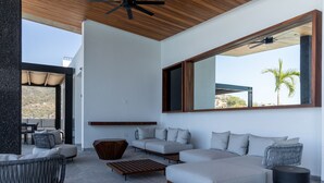 Una sala de estar moderna con un ventanal grande, un ventilador de techo y una zona de estar con sofás y una mesa de centro.