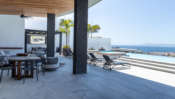 Un área de estar moderna al aire libre con piscina, que presenta techo de madera, pilares de piedra y vista al océano.