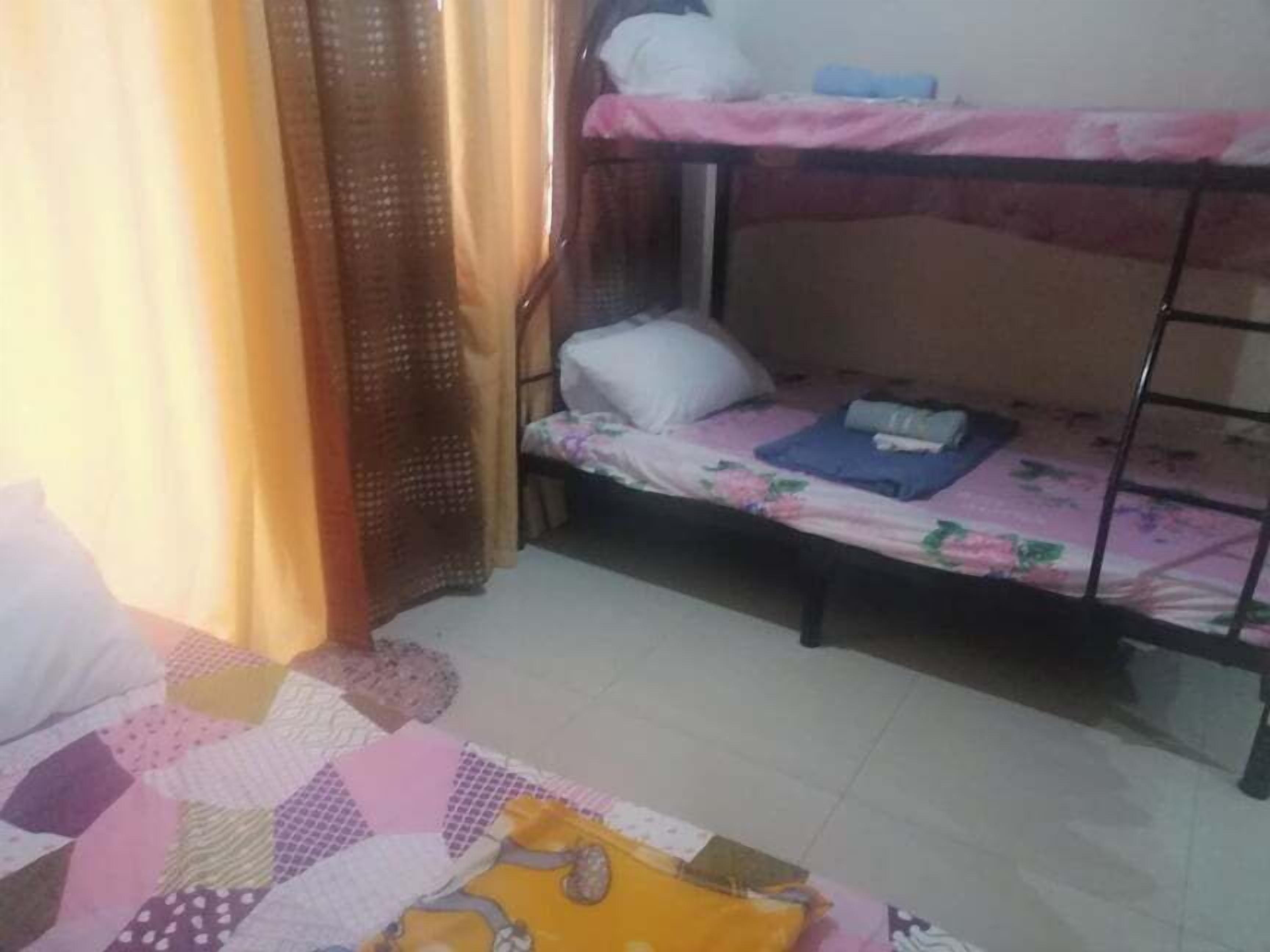 A dormitory room with bunk beds, a quilt on the lower bed, and a curtain partially drawn.