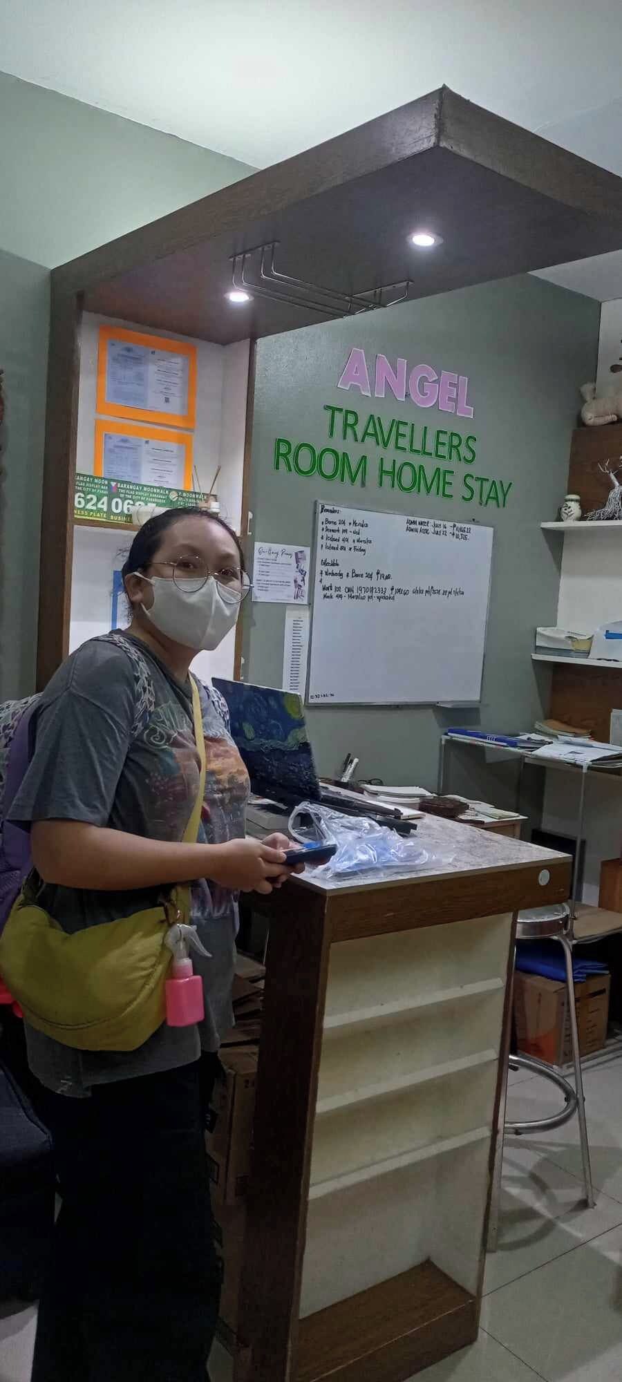 A reception desk with a sign for 'ANGEL TRAVELLERS ROOM HOME STAY' and a whiteboard with handwritten notes.