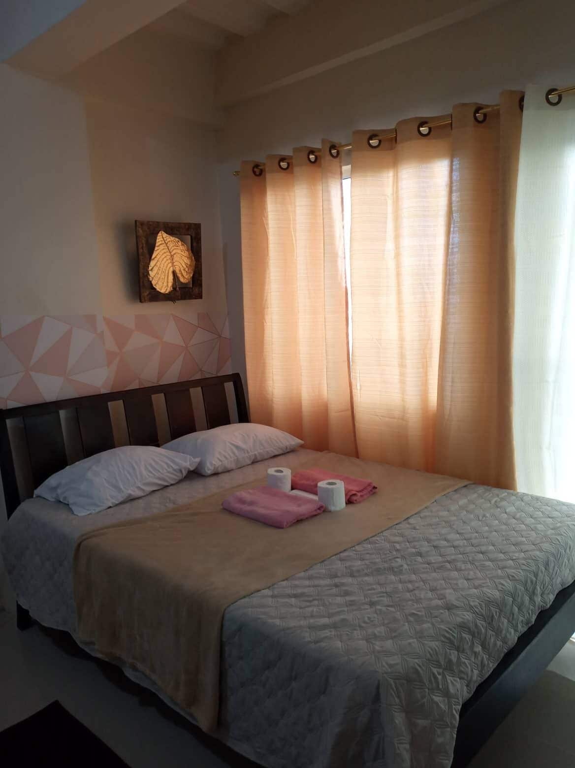 A neatly made bed with a quilted bedspread, two pillows, and a pair of pink towels.
