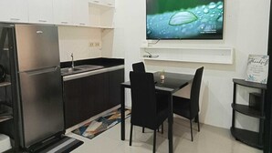 A compact kitchen with a refrigerator, sink, and a TV mounted on the wall displaying a nature scene. - ANGEL ROOM HOMESTAY AT KASSEL RESIDENCES (Parañaque)