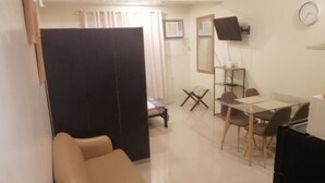 A living room with a sofa, a dining table with chairs, a TV mounted on the wall, and a clock. - ANGEL ROOM HOMESTAY AT KASSEL RESIDENCES (Parañaque)