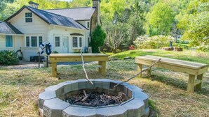 A house with a fire pit in the yard, surrounded by benches and a garden.