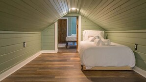 A bedroom with a sloped ceiling, a wooden floor, and a bed with white bedding.