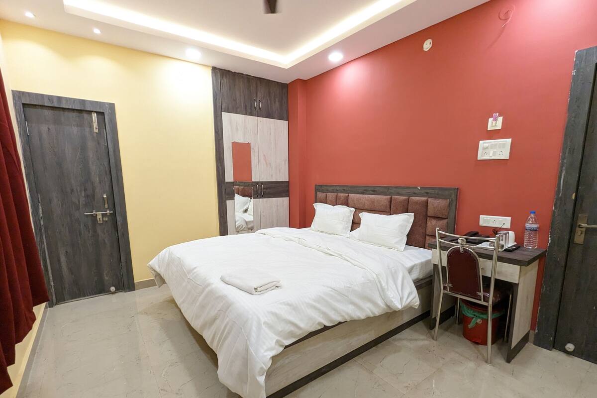 A hotel room with a bed, a desk, a chair, and a water bottle.