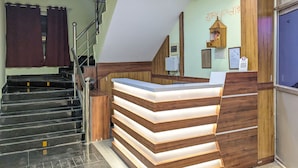 A reception desk with a wooden finish and a glass top, a staircase with metal railings, and a wall-mounted security camera.