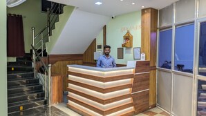 A reception desk with a staircase leading to an upper floor, a wall-mounted fan, and a window with a view.