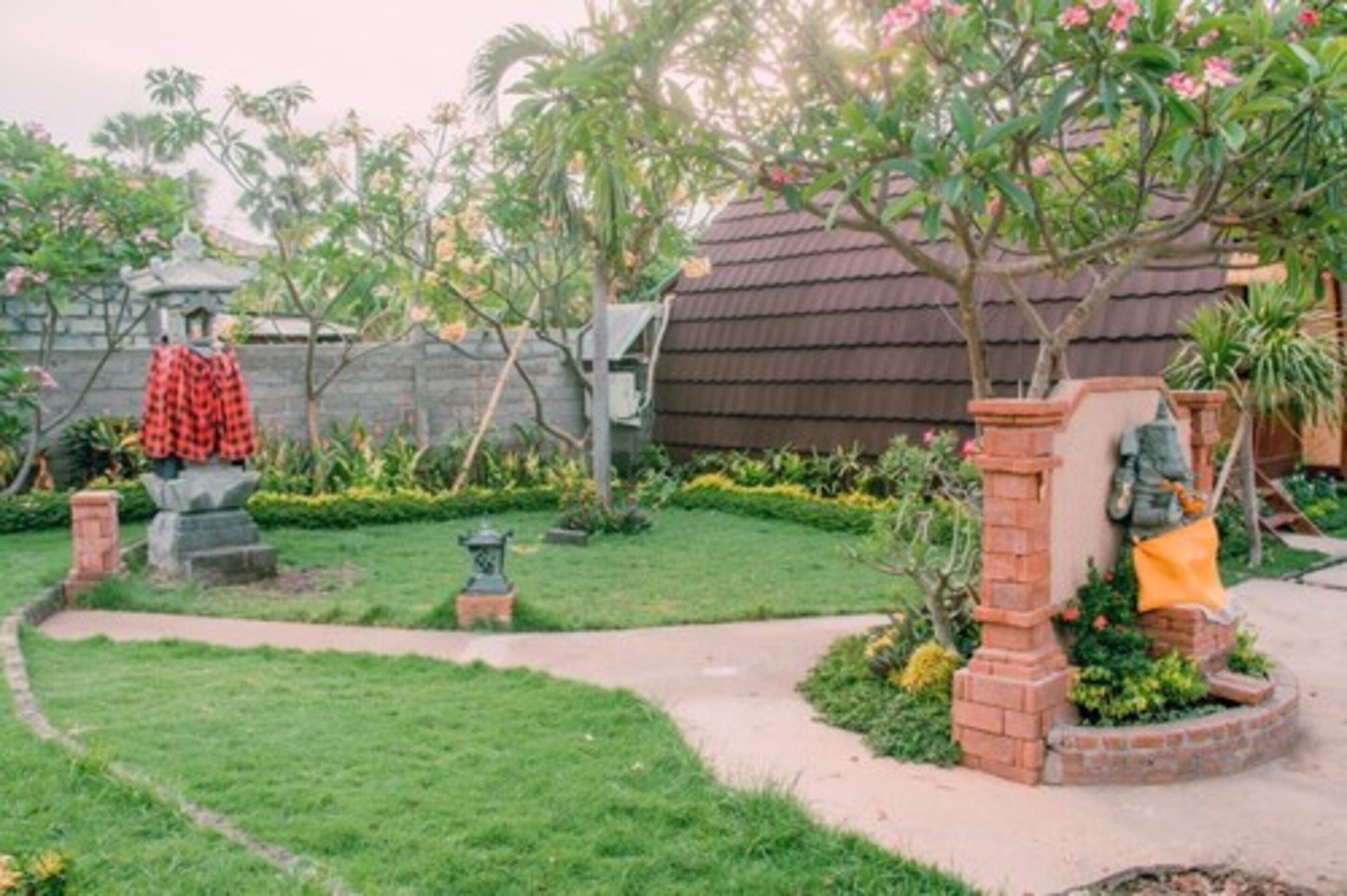 Un jardín con un sendero, una construcción de techo de paja y diversas plantas y elementos decorativos.