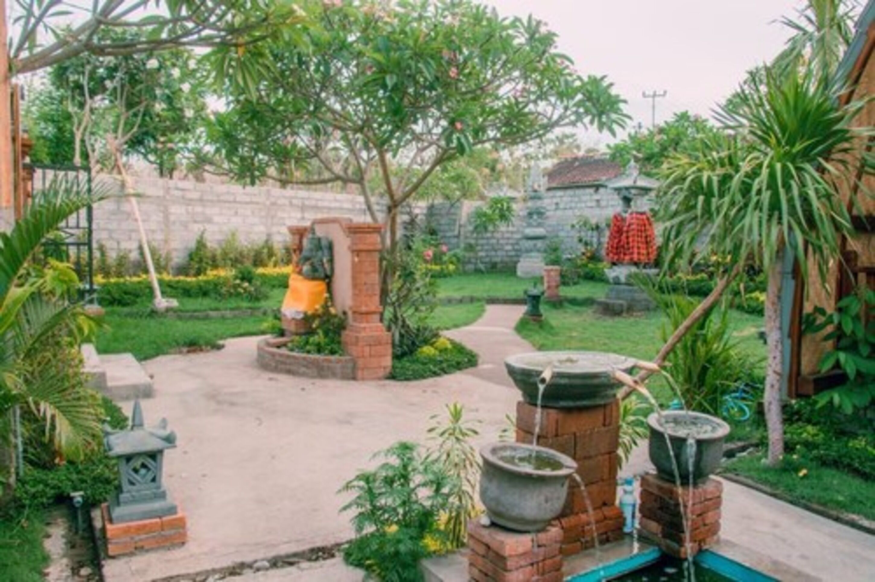 Un jardín con un camino de ladrillo, plantas en macetas y una fuente tradicional.