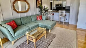 A living room with a sectional sofa, a small wooden coffee table, and a kitchen in the background. - Tranquility on West Moloka'i (Maunaloa)