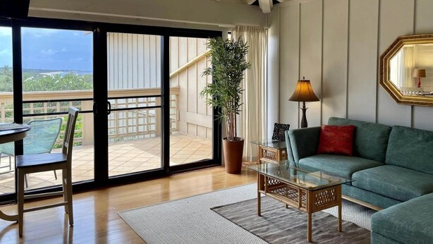 A spacious living area with a large sliding glass door leading to a balcony, a green sofa, a glass coffee table, and a potted plant. - Tranquility on West Moloka'i (Maunaloa)