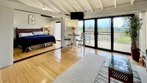 A spacious room with a large bed, a small table, a chair, and a balcony with a view. - Tranquility on West Moloka'i (Maunaloa)