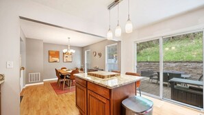 A modern kitchen with a large island, wooden cabinets, and a dining area with a red rug. - NEW! 3 Bdrm | Mt Washington | Garage (Pittsburgh)