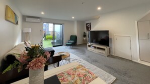 Ein modernes Wohnzimmer mit einer Couch, einem Fernseher und einer Schiebeglastür, die zu einem Garten führt.