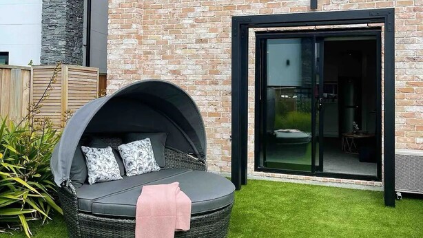 Ein modernes Haus mit Ziegelaußenwand, einer großen Glas-Schiebetür und einem runden Sitzbereich im Freien mit Kissen.