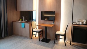 Una habitación de hotel moderna con kitchenette, un televisor de pantalla plana en la pared y una pequeña zona de comedor con dos sillas.