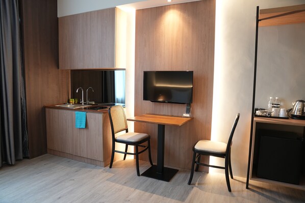 A modern hotel room with a kitchenette, a flat-screen TV mounted on the wall, and a small dining area with two chairs. - Roxy Hotel Aiman (Kota Samarahan)