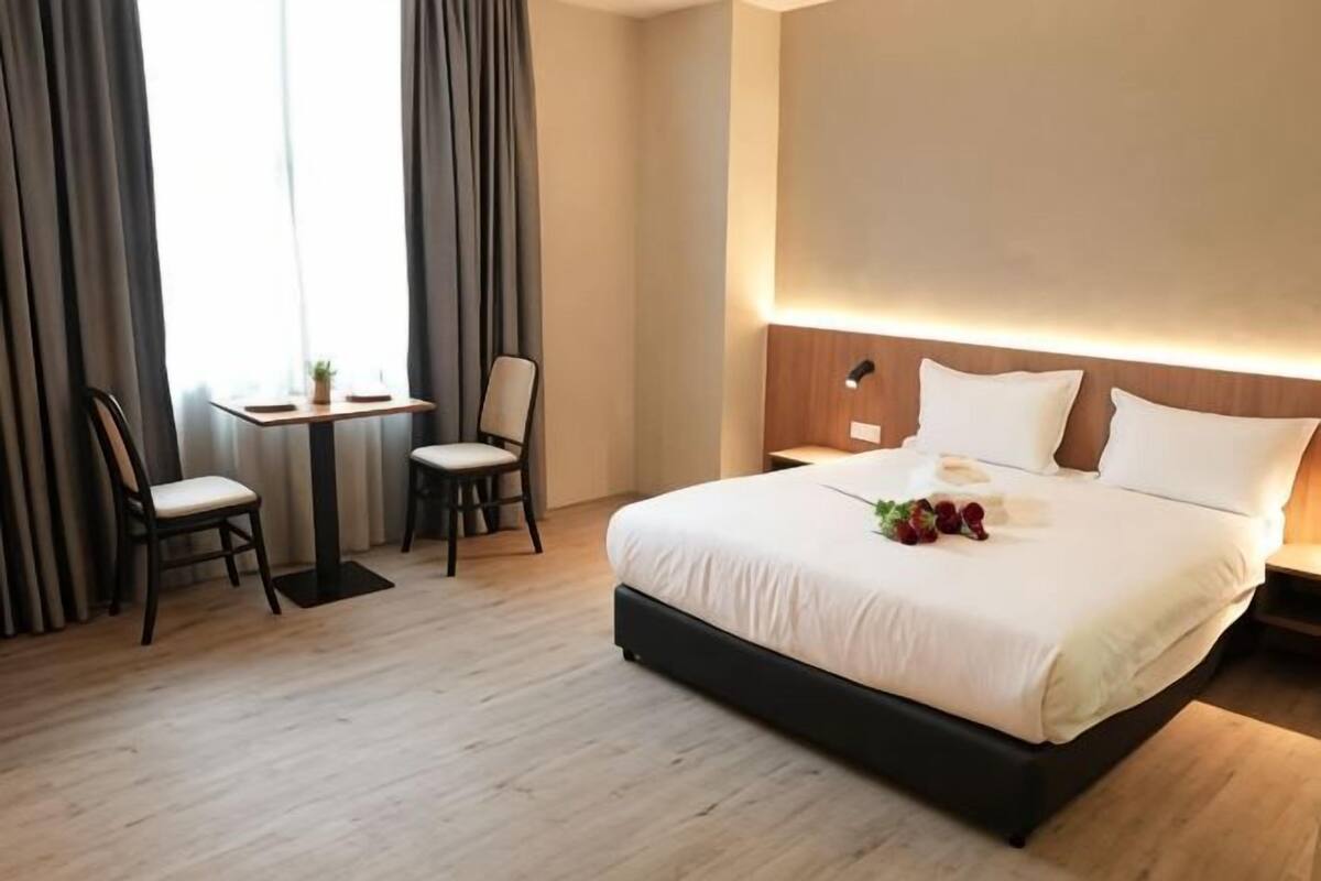 A hotel room with a bed, two chairs, a small table, and a nightstand.